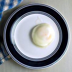 an egg on a black and white plate next to a blue checkered napkins