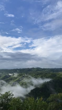 the clouds are rolling in over the trees and mountains on a sunny day with blue skies