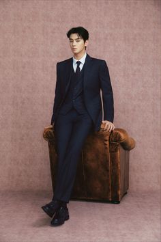 a man in a suit and tie sitting on top of a brown chair with his legs crossed