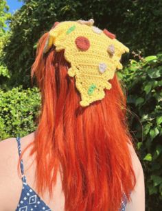 a woman with long red hair wearing a crocheted sunflower headband in front of trees