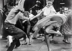 two people are dancing in front of a group of people on the floor with their arms outstretched