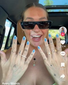 a woman with blue fingernails is smiling and holding her hands up to the camera while wearing sunglasses