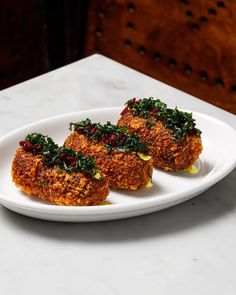 three crab cakes on a white plate sitting on a marble counter top, ready to be eaten