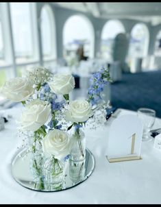 white roses and blue flowers in glass vases on a table at a wedding reception