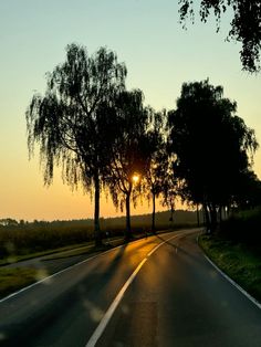 the sun is setting behind some trees on the side of the road with no cars