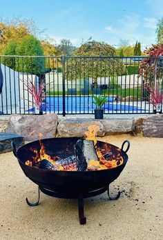 a fire pit sitting on top of a cement ground next to a fence and swimming pool