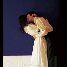 a man and woman kissing in front of a blue wall