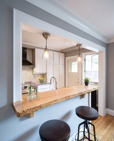 two stools are sitting at the bar in this modern kitchen with white cabinets and wood countertops