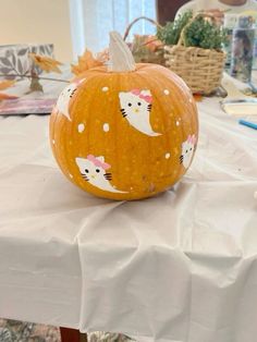 a pumpkin with cats painted on it sitting on top of a white tablecloth covered table