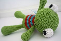 a crocheted green stuffed animal laying on top of a white table next to a red and blue object