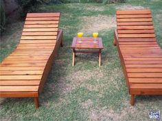 three wooden lounge chairs sitting on top of a grass covered field next to a small table