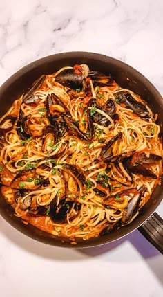 a pan filled with pasta and mussels on top of a white marble counter