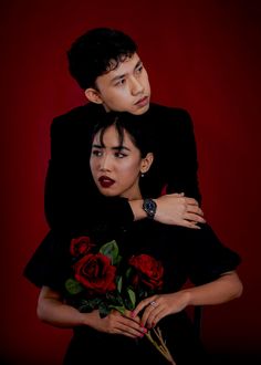 a man and woman embracing each other with red roses in their lap, against a dark background