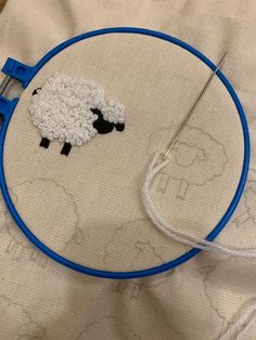 a blue hoop with a white sheep on it next to a needle and thread holder