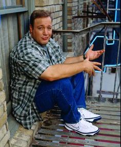 a man sitting on the side of a building with his hands out and looking at the camera