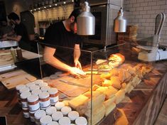 a man preparing food in a kitchen behind a glass counter with cups on the side