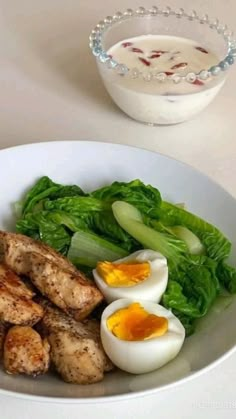 a white plate topped with meat and veggies next to a bowl of dressing