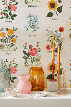 various vases and candles on a table with flowers painted on the wall behind them