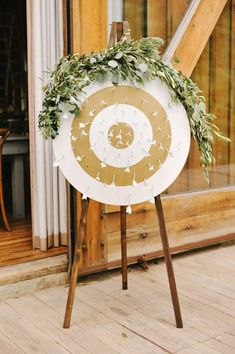 a white and gold sign with greenery on it sitting in front of a window