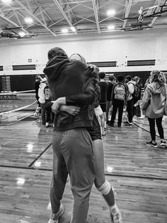 two people hugging each other while standing on a wooden floor in an indoor gym area