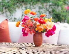 a vase filled with colorful flowers sitting on top of a wicker table next to pillows