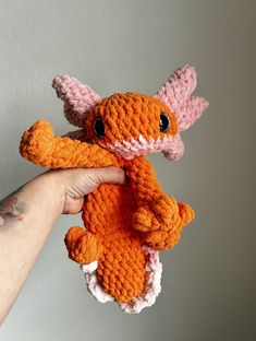 a hand holding an orange and pink crocheted stuffed animal in it's palm