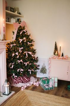 a decorated christmas tree with pink bows in a living room next to a fire place