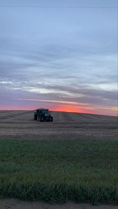 a tractor in the middle of a field at sunset