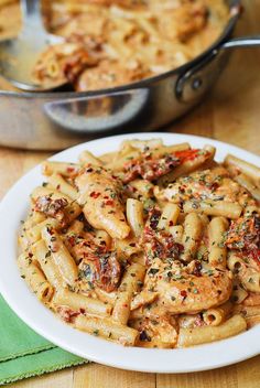 a white plate topped with pasta and sauce next to a pan filled with other food