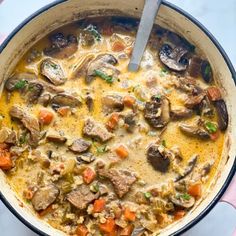 a pot filled with meat and vegetables on top of a table next to a spoon