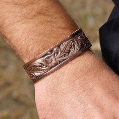 Details From the Leather Cut Collection, a copper finished cuff bracelet with a precisely hand painted backdrop creates a leather-like piece. Created with idea of transforming leather into metal this bracelet focuses on the distinctive Sheridan style. Copper finishing highlights the edges of buck stitching framing the edges of the bracelet. The hand painted black contrasts and highlights the bright-cut copper-toned floral and leaf Sheridan leather carving pattern. Dimensions Width 0.740000 Heigh Bracelets Western, Hand Painted Backdrop, Western Cuff Bracelet, Western Items, Mens Copper Bracelet, Mens Leather Jewelry, Floral Engraving, Western Bracelets, Pewter Art