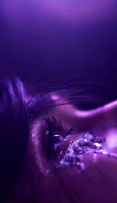 a close up of a person's eye with purple light shining on her face