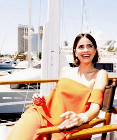 a woman in an orange dress is sitting on a chair near the water and boats