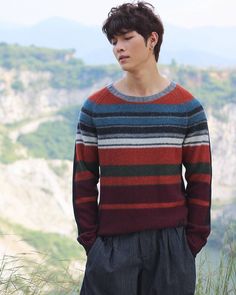 a young man standing on top of a grass covered hillside wearing a striped sweater and pleated shorts