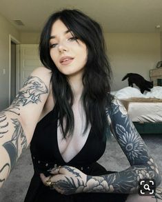 a woman with tattoos on her arms and chest posing for a photo in front of a bed