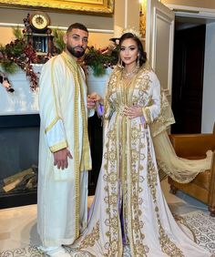 a man and woman standing next to each other in front of a fire place wearing traditional clothing