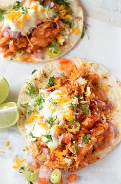 two tacos with shredded meat and vegetables on them next to a lime wedges