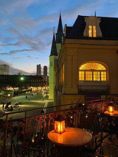 a balcony with tables and chairs on it at night, lit up by lights in the windows