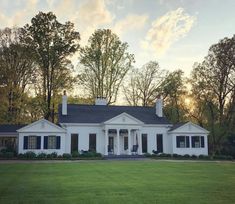 a white house with black shutters in the front yard and trees on either side