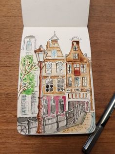 a notepad with a drawing of buildings and a street light on it next to a pen