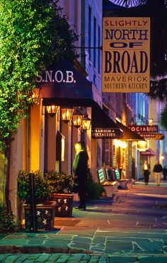 the sidewalk is lit up at night with people walking down it and shops on both sides