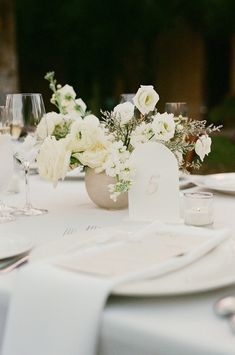 the table is set with white flowers, candles and place settings for an elegant dinner