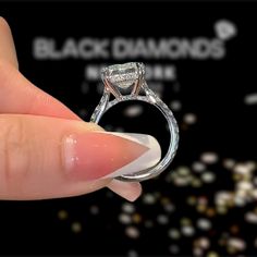 a hand holding a diamond ring in front of a black background