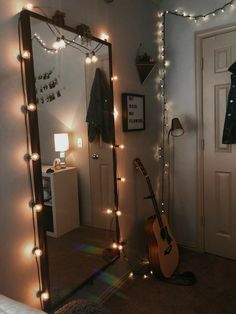 a guitar is sitting on the floor in front of a mirror with lights around it