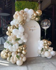 balloons and greenery decorate the entrance to a wedding reception in gold and white colors