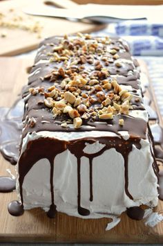 a cake with white frosting and chocolate drizzled on top, sitting on a wooden cutting board