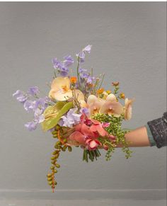 a person holding a bouquet of flowers in their left hand, with the background gray wall behind them