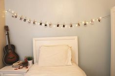 a white bed topped with pillows next to a string of lights and a wooden guitar