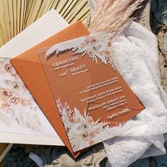 an orange and white wedding card with feathers on it next to some fan shaped fans