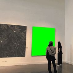 two people looking at paintings in an art gallery with green screen on the wall behind them